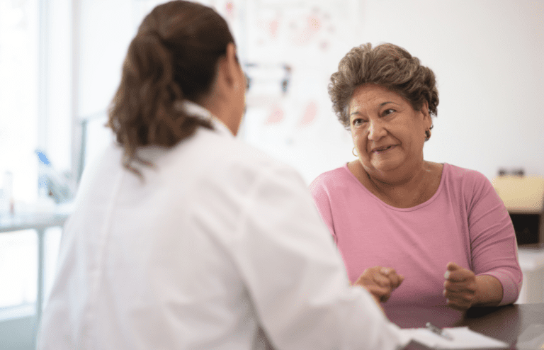 Doctor with back to camera talking to an older woman with short hair and wearing a pink top