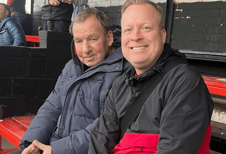 John Mills and David Watts in the stands at a recent home game for Maltby Main FC. Both are wearing big coats and are smiling