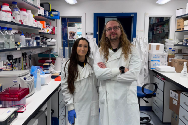 Lewy Body Society funding: woman and man both with long hair and wearing white coats standing in a lab