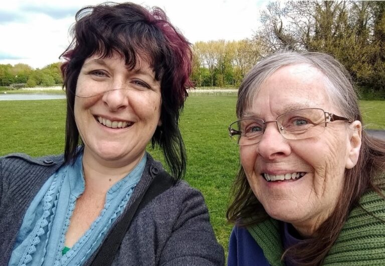 Carers Week: Louise Yates with dark hair and her mum Marion who has grey hair and glasses smiling outdoors in a park